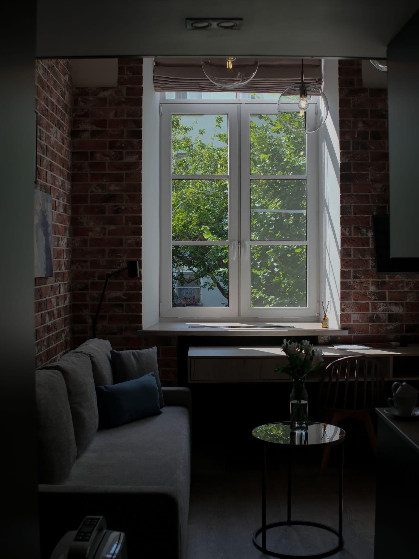 A brick-walled Brooklyn living room with a sofa beneath a tall window